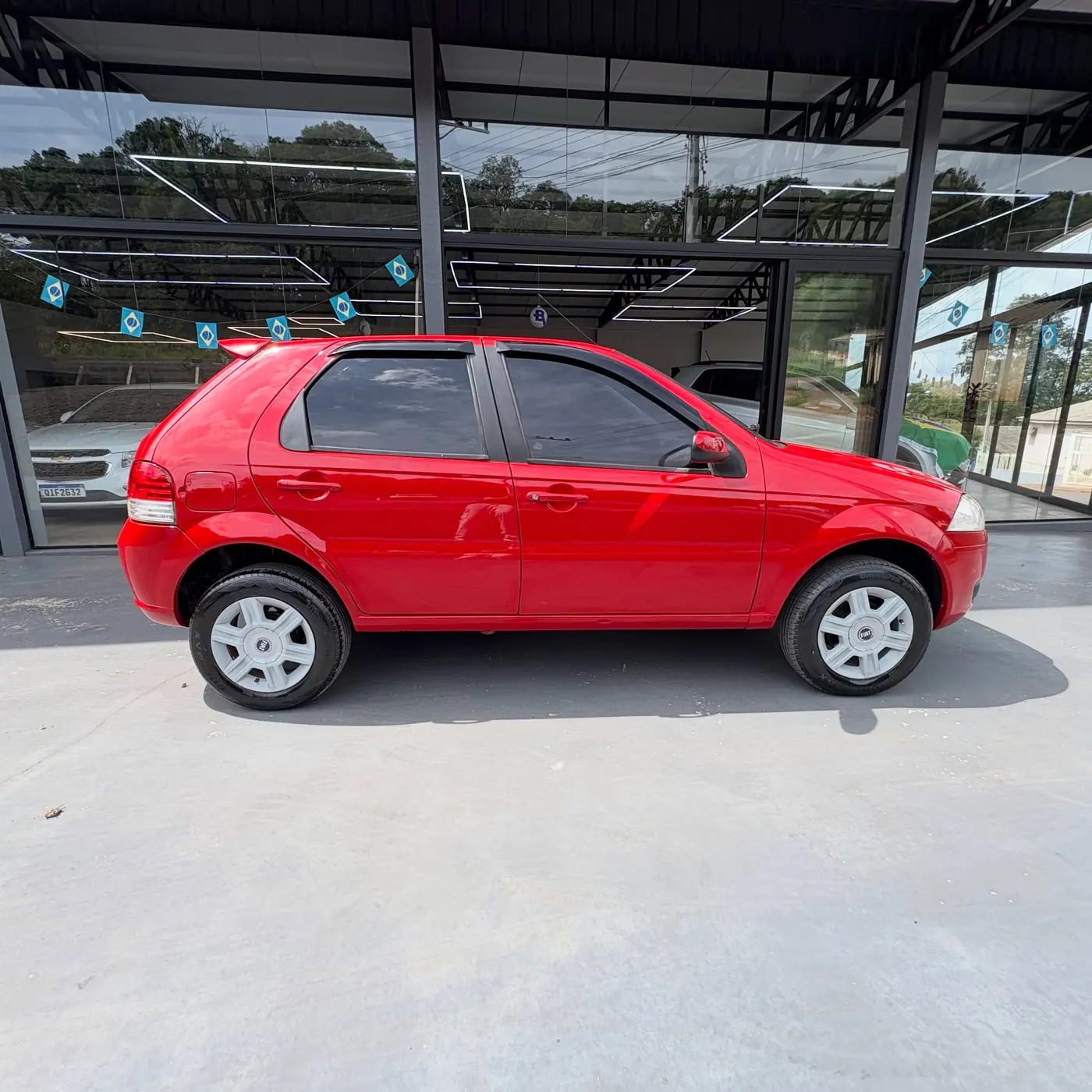 Fiat Palio vermelho na frente do salão envidraçado da Multimarcas Veículos